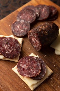 several slices of salami sitting on top of a wooden cutting board next to cheese