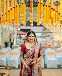 a woman in a red and gold bridal gown standing under an archway decorated with yellow garlands