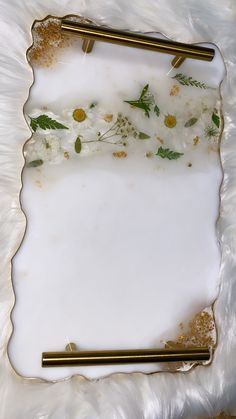 an empty white plate with gold handles and some flowers on it, sitting on a furnishing