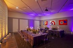 a large room with purple lighting and long tables set up for a formal dinner or party