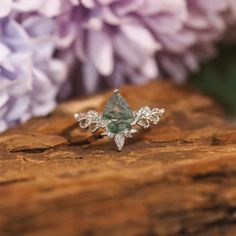 a green ring sitting on top of a piece of wood next to purple and white flowers