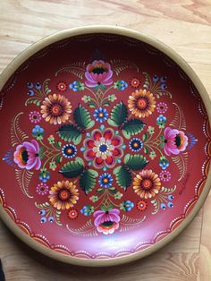 a red bowl with colorful flowers painted on the bottom and sides, sitting on a wooden table