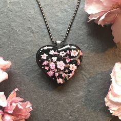 a black heart shaped necklace with pink flowers on it next to a flowery branch