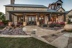 a large stone house with lots of flowers in the front yard and landscaping around it