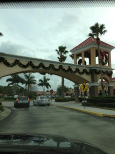 cars driving under an arch decorated with christmas lights and garlands in front of a shopping center