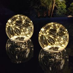 two glass orb lights sitting on top of a reflective surface in front of a dark background