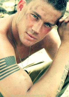 a man with an american flag tattoo on his arm and chest sitting in the woods