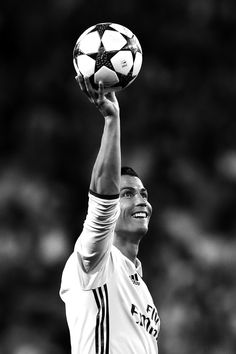 a man holding a soccer ball up in the air with his right hand on top of it