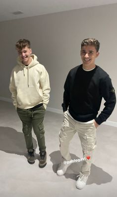 two young men standing next to each other in an empty room with white walls and flooring