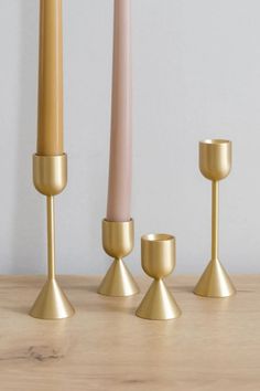 three gold candles are lined up on a wooden table with one candle in the middle