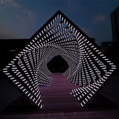 an abstract sculpture is lit up in the dark with white lights on it's sides