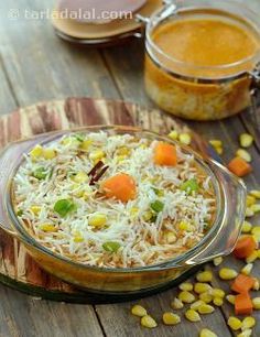 a glass bowl filled with rice and vegetables on top of a wooden table next to two jars