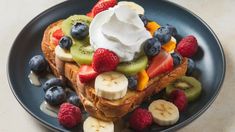 a blue plate topped with french toast covered in whipped cream and fresh fruit on top