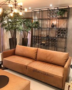 a tan leather couch sitting in front of a window next to a wooden table and chair