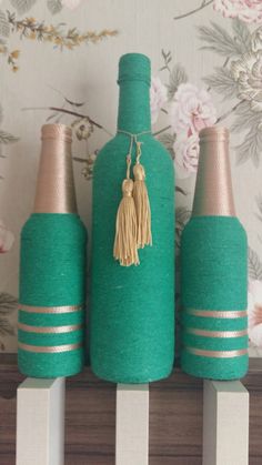 three green bottles with tassels on them sitting on top of a wooden shelf