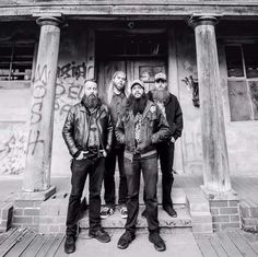 black and white photograph of four men standing in front of an old building with graffiti on it