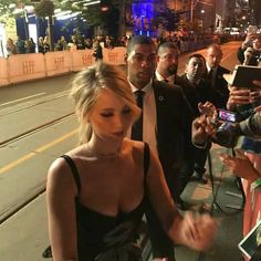 a woman in a black dress signing autographs for fans on the street at night