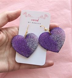 "Big purple and silver heart earrings, glittery, sparkly, wide, resin, cute, feminine, love themed earrings Resin earrings also include resin dye and may include sequins, sparkles, plastic decals, glass, plastic gems, rhinestone stickers, glitter, and/or real dried flowers. All of the hooks are hypoallergenic. Earrings may also be painted with acrylic paint.  The earrings you see listed are one of a kind and are an already made, finished product (unless it says \"made to order\"). The pairs are Silver Heart Earrings For Party, Purple Earrings For Valentine's Day, Purple Heart-shaped Jewelry For Party, Purple Heart-shaped Earrings For Pierced Ears, Heart Shaped Purple Jewelry For Party, Purple Heart-shaped Pierced Earrings, Heart-shaped Purple Jewelry For Party, Cute Purple Earrings For Party, Cute Purple Party Earrings