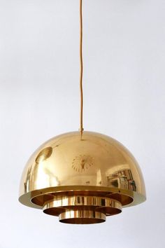 a gold colored pendant light hanging from a ceiling fixture with a white wall in the background