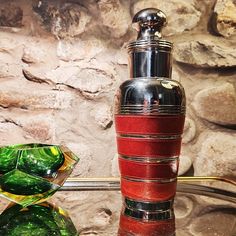 a red and green vase sitting on top of a glass table next to a stone wall