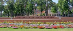 the university of south alabama sign is surrounded by colorful flowers and trees in front of it