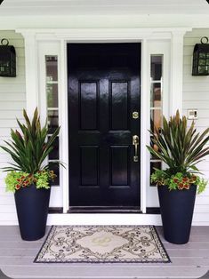 two large planters are on the front steps of a white house with black doors