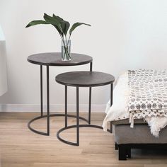 two round tables with plants in them on the floor next to a bed and nightstand