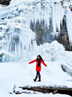 a woman standing in front of a waterfall covered in ice and snow with her arms outstretched