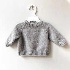 a gray sweater hanging on a white hanger against a white wall with a clip to the front of it