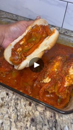 a person holding a hot dog in a bun on top of a pan filled with sauce