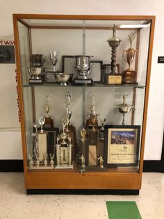 a display case filled with trophies and plaques on top of a green mat in front of a wall