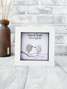 a couple of rocks sitting inside of a white frame next to a vase with reeds