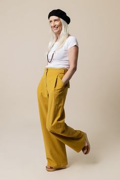 a woman in yellow pants and a black hat is posing for the camera with her hands on her hips