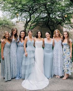 a group of women in dresses standing next to each other on a sidewalk with trees behind them