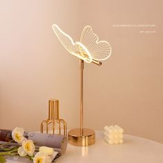 a table topped with a lamp next to flowers and magazines on top of a white table