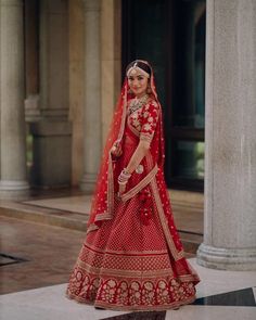 a woman in a red and gold bridal gown posing for the camera with her hand on her hip