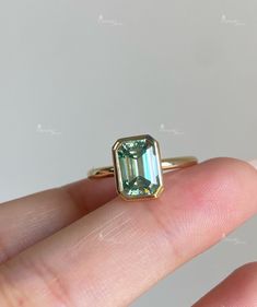 a close up of a person's hand holding an emerald ring