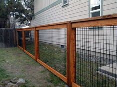 a fence that is next to a house with grass and rocks on the ground in front of it