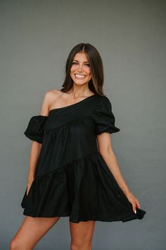 a smiling woman in a black dress posing for a photo with her legs crossed and one leg up