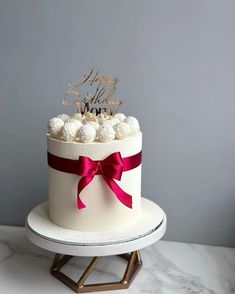 a white cake with red ribbon and gold lettering on top, sitting on a stand