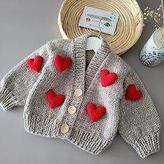 a knitted sweater with red hearts on it next to a basket and vase filled with flowers