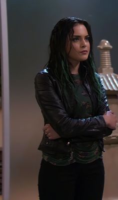 a woman standing with her arms crossed wearing a black leather jacket and jeans, looking at the camera