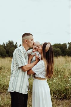 a man and woman kissing their baby while standing in a field