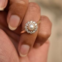 a woman's hand holding a ring with a pearl and diamonds on the side