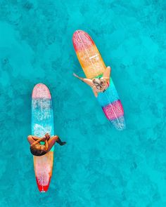 two people are floating on surfboards in the blue water, one is upside down