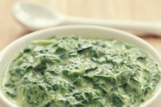 a white bowl filled with green food on top of a wooden table