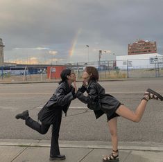 two young women are kissing on the street with a rainbow in the sky behind them