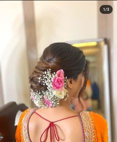 the back of a woman's head with flowers in her hair and an orange blouse