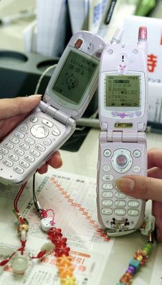 two people holding open flip phones on top of a table with chinese characters written on them