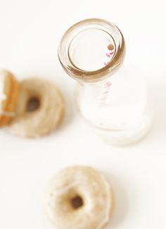 two doughnuts sitting next to a glass jar on a white surface with the lid open